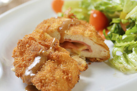 Cordon bleu mit knuspriger Panade und geschmolzenem Käse, serviert mit frischem Salat auf einem Teller
