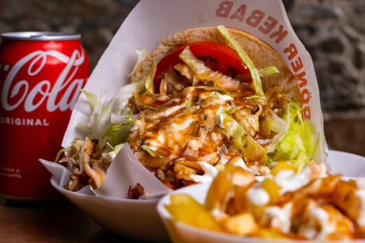 Kebap mit Fleisch, Salat und Sauce in einer Box serviert, daneben eine Cola Dose