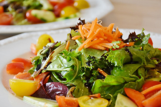 Frischer gemischter Salat mit Blattsalat, Karotten, Tomaten und Oliven auf einem Teller angerichtet
