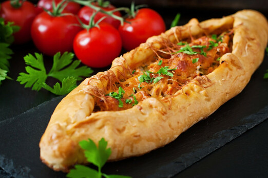 Frisch gebackene Pide mit Fleischfüllung und Kräutern, serviert auf einer dunklen Platte
